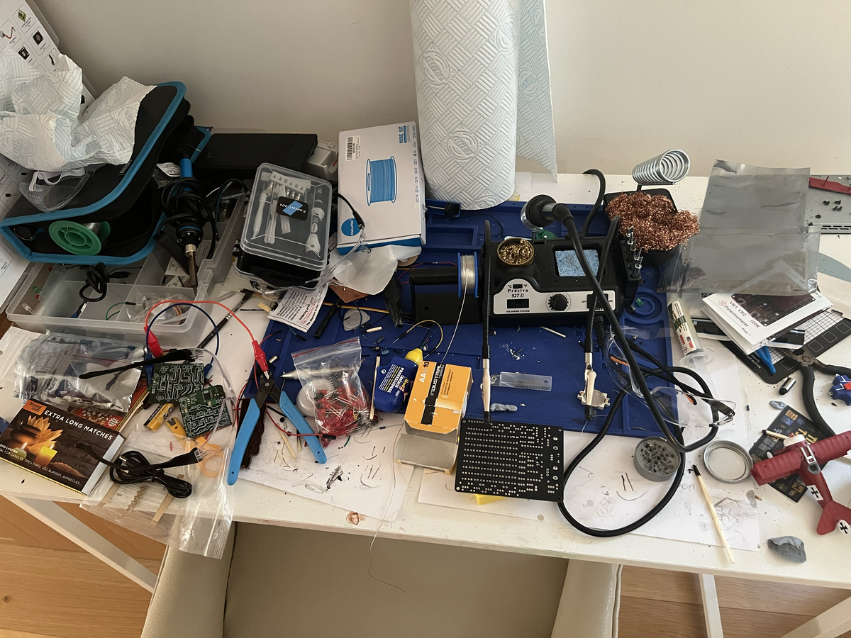 Nathan's real hardware hacking bench — a cluttered desk of soldering station, probe clips, perfboard, components, wire and tools