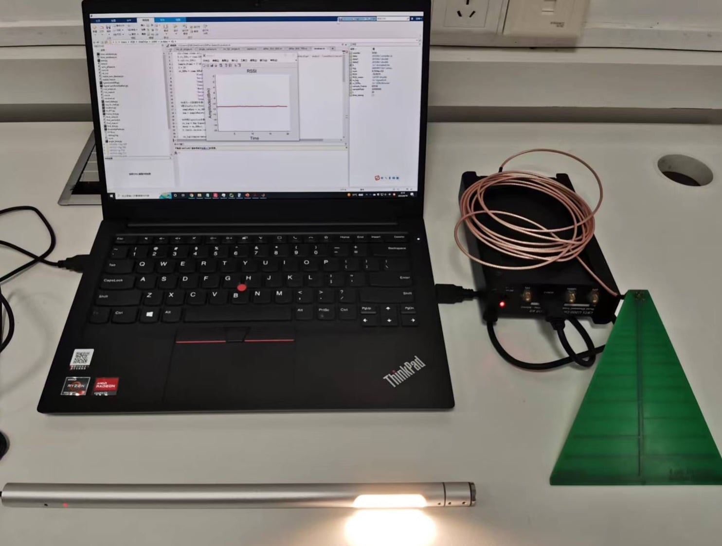 The ESauron prototype: a laptop, USRP B210 software-defined radio, log-periodic antenna and strobe light on a desk. Image: Zhang et al., USENIX Security 2024